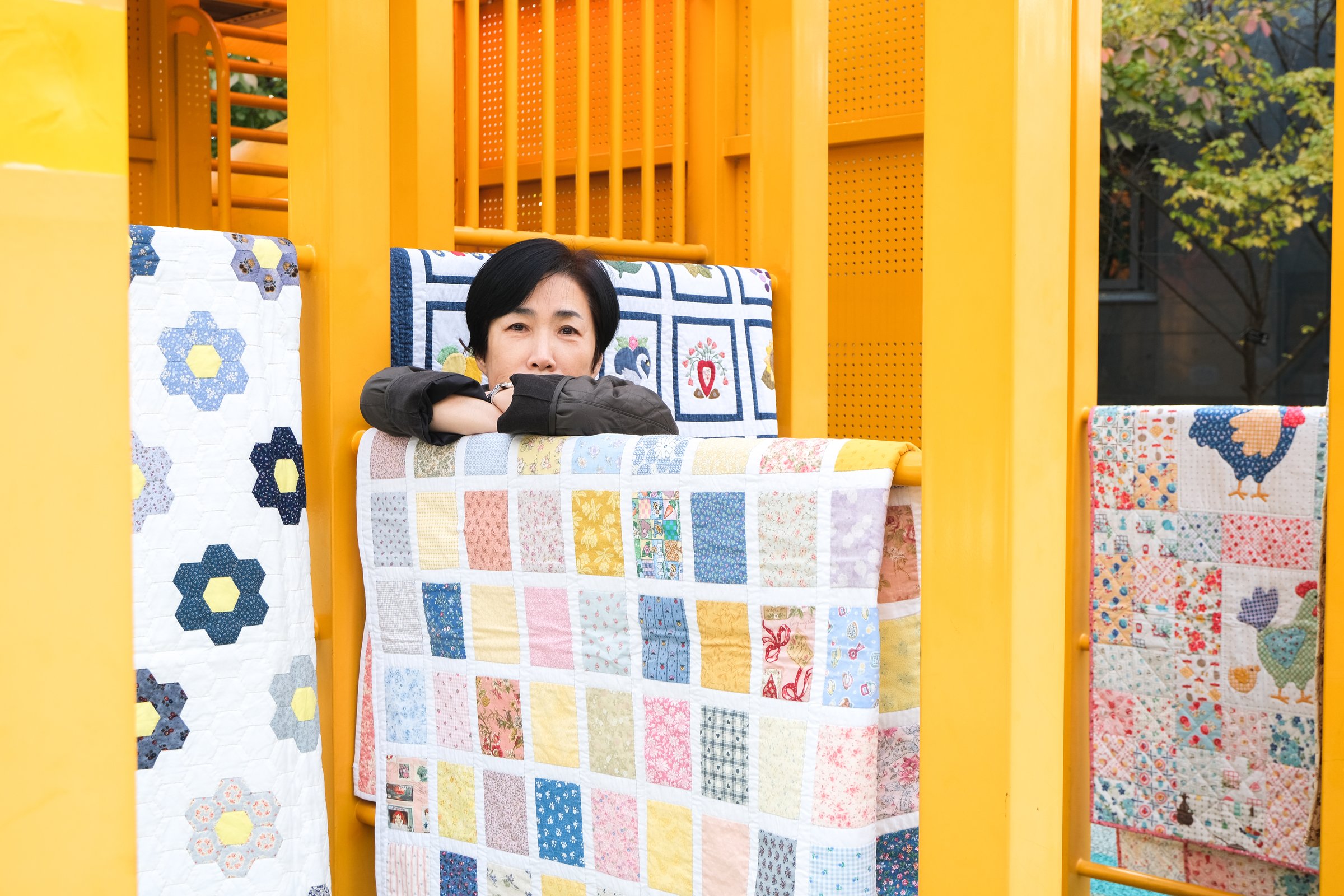 Kim Minseon standing behind several handmade quilts outdoors.
